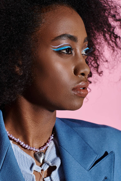 Stylowa młoda Afroamerykanka z kręconymi włosami pozuje w niebieskim garniturze i dopasowuje makijaż. - Zdjęcie, obraz