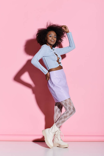 Uma jovem mulher afro-americana elegante com cabelo encaracolado, marcando uma pose graciosa na frente de uma parede rosa vibrante. - Foto, Imagem