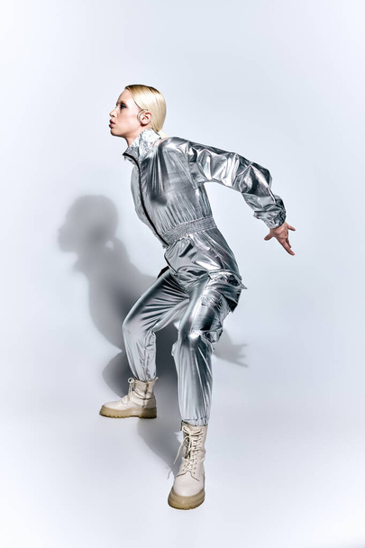 beautiful woman in silver futuristic attire posing in motion on gray backdrop and looking away - Фото, зображення