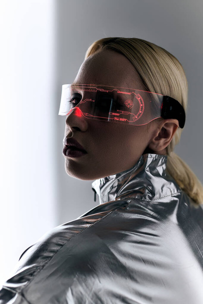 extraordinary woman with sci fi glasses in robotic clothing looking at camera on gray backdrop - Photo, Image