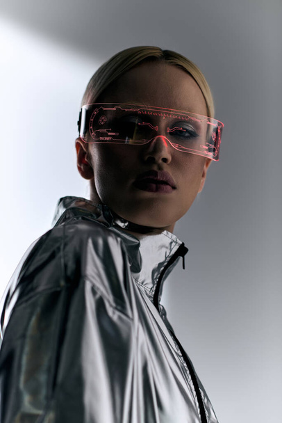 extravagant woman with sci fi glasses in robotic silver clothing looking at camera on gray backdrop - Foto, Bild