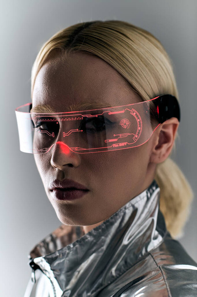 appealing blonde woman with futuristic glasses in silver outfit looking at camera on gray background - Фото, зображення