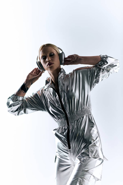 appealing bizarre female model with headphones wearing silver robotic attire and enjoying music - Foto, afbeelding