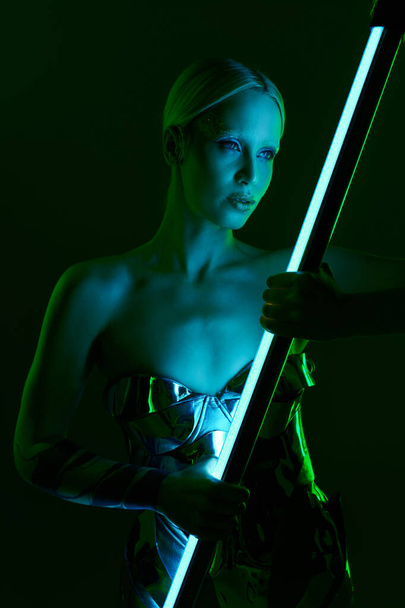 青いLEDランプの棒を握る金属のロボットの衣装の並外れた女性および遠く見て - 写真・画像