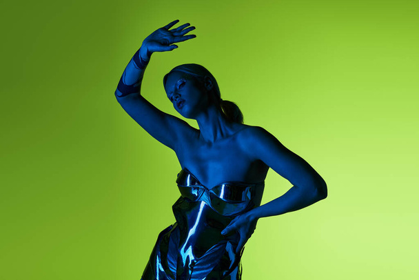 eigenaardige verleidelijke vrouw in futuristische sci fi kleding rusten in blauw licht op groene achtergrond - Foto, afbeelding