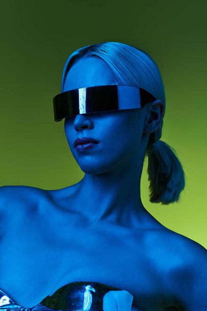 extravagante Frau in silberner Roboterkleidung mit Science-Fiction-Sonnenbrille posiert in Lichtern vor grünem Hintergrund - Foto, Bild