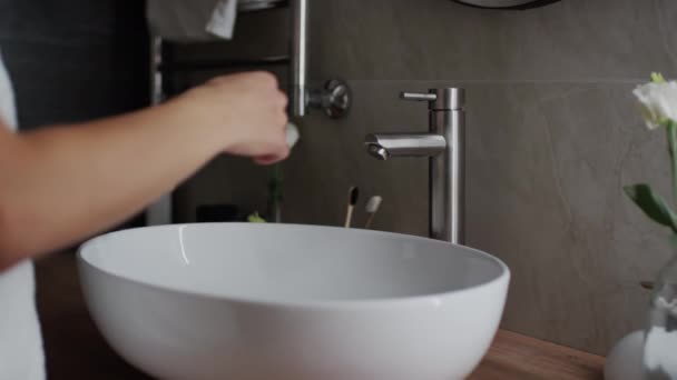Plan rapproché moyen des mains et du milieu d'une jeune femme méconnaissable portant une serviette de bain marchant jusqu'au lavabo, soulevant le robinet et se lavant les mains sous l'eau courante - Séquence, vidéo