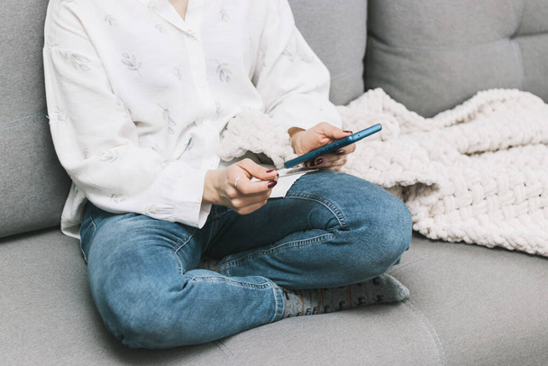 Nierozpoznawalna kobieta siedząca na kanapie, trzymająca kartę kredytową i korzystająca z telefonu komórkowego, smartfona do zakupów online lub płatności przez internet. - Zdjęcie, obraz