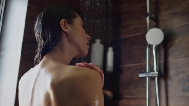 朝シャワーで洗濯する若い白人女性のミディアムクローズアップ後部ショットと穏やかな円形の動きで裸の肩の上に石鹸を広げる - 映像、動画