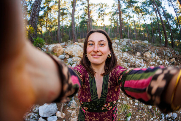 Ευτυχισμένο κορίτσι σε ένα φόρεμα παίρνει μια φωτογραφία της σε ένα smartphone στο πάρκο. νεαρή κοπέλα που παίρνει selfie στο δάσος - Φωτογραφία, εικόνα