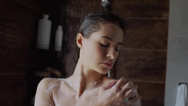 Primo piano slow shot di sensuale giovane donna caucasica lavata con sapone nella doccia al mattino, toccando e accarezzando spalle nude, petto e collo, ad occhi chiusi, sognando qualcosa di piacevole - Filmati, video