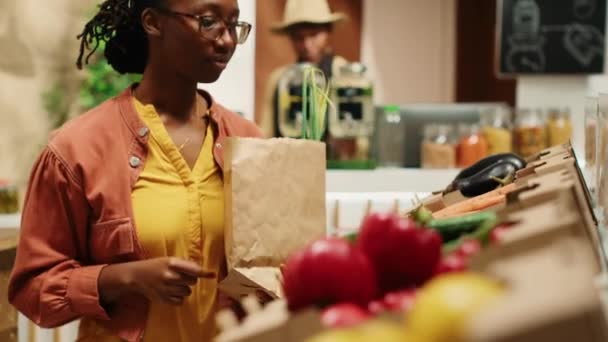 Pravidelný klient dává bio domácí zeleninu do papírové tašky, nakupuje v obchodě s ekologickým odpadem. Žena podporující malé podniky a udržitelný životní styl. Fotoaparát A. Handheld shot. - Záběry, video