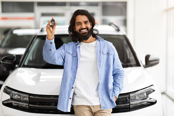 Emocionado bonito barbudo milenar indiano cara de pé ao lado de novo carro branco, mostrando a chave do novo automóvel de luxo e sorrindo, comemorando a compra na concessionária de automóveis - Foto, Imagem