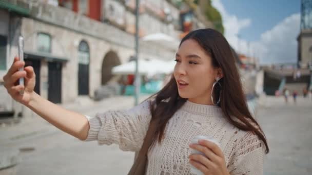 Turista nő, hogy szelfi kávéscsészével a nagy városi kilátás közelkép. Stílusos ázsiai lány okostelefonnal fotózza magát a nyári hétvégén. Pozitív mosolygós barna pózol a napos utcán - Felvétel, videó