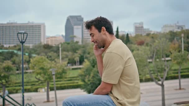 Vrolijke man beëindigen oproep ontspannen op stadspark bank close-up. Lachende Spaanse man hing smartphone tevreden vriendelijk gesprek buiten. Gelukkig mannelijk toerist genieten weekend rust op groen plein. - Video