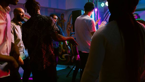 Diversas personas de fiesta en el club nocturno, disfrutando de la fiesta disco en la pista de baile con música DJ fresco. Hombres y mujeres sonrientes divirtiéndose juntos en la discoteca, evento de celebración. Disparo de mano. - Foto, Imagen