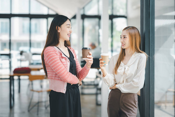 Business relax koncept, dvě asijské podnikatelek těší příležitostný rozhovor s šálky kávy v jasné, moderní kancelářské chodbě. - Fotografie, Obrázek