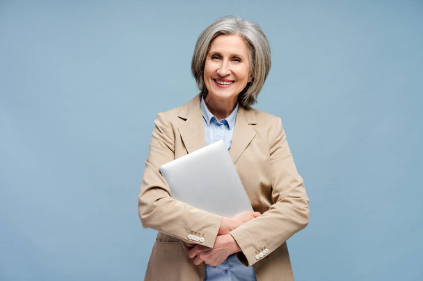 Portret lachende oudere vrouw, manager, werknemer met laptop kijkend naar camera geïsoleerd op blauwe achtergrond - Foto, afbeelding