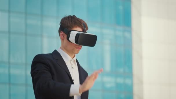 Инженер-мужчина носит гарнитуру виртуальной реальности и Жесты в дополненной реальности, стоя рядом со зданием с голубыми окнами. Трансформация. - Кадры, видео