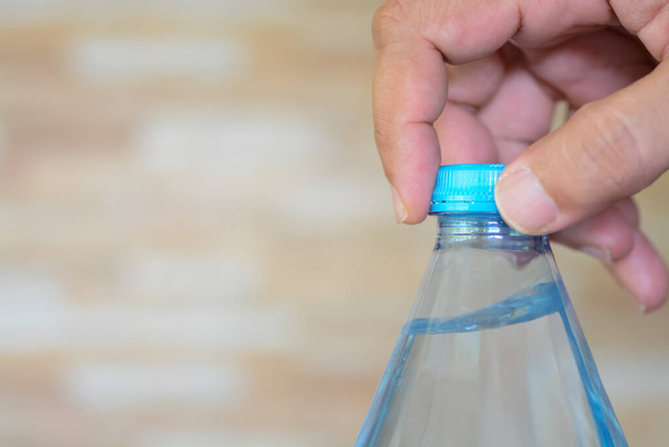 απαλά τα χέρια ανοίγουν το καπάκι ενός δροσιστικού μπουκαλιού με νερό, έτοιμο να σβήσει τη δίψα. - Φωτογραφία, εικόνα