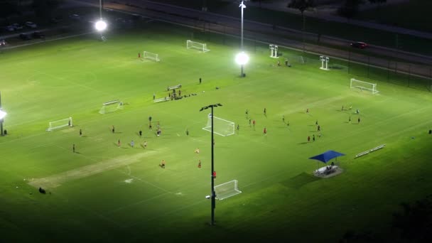 Arena de deportes públicos iluminados en North Port, Florida con personas que juegan al fútbol en el estadio de fútbol de hierba por la noche. Concepto actividades al aire libre. - Metraje, vídeo