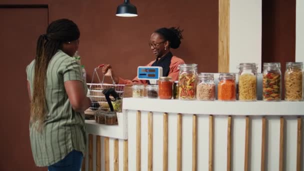 Африканская американка покупает свежесобранную продукцию в местном продуктовом магазине в поисках натуральных спелых фруктов и овощей. Торговец взвешивает товар по шкале для клиента. Портативный выстрел. - Кадры, видео
