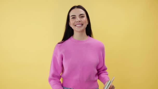 Schattige vrouw die op een gele achtergrond staat en copybooks in handen houdt. capabele universitaire student in roze kleding gevoel enthousiast over nieuw studiejaar en klaar om nuttige kennis te krijgen. - Video