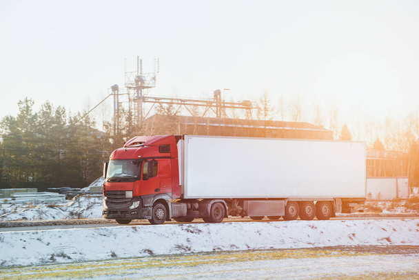 Ένα μεγάλο φορτηγό μεταφοράς μεταφέρει εμπορικό φορτίο σε έναν χιονισμένο αυτοκινητόδρομο. Το ημιρυμουλκούμενο αντιμετωπίζει επικίνδυνη χιονοθύελλα και ολισθηρές οδικές συνθήκες. - Φωτογραφία, εικόνα