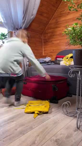 Vertikal aufgenommen versteckt sich ein entzückendes Mädchen im Teenageralter spielerisch in einem Koffer, während sich ihre Eltern auf einen Urlaub vorbereiten. Das Konzept der Familienurlaubsvorbereitungen, Spaß und Spannung im Wohnkomfort - Filmmaterial, Video