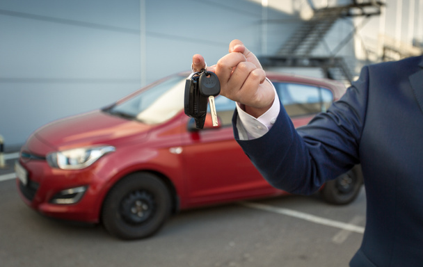 Closeup του διευθυντή πωλήσεων, κρατώντας τα κλειδιά του αυτοκινήτου κατά το νέο αυτοκίνητο - Φωτογραφία, εικόνα