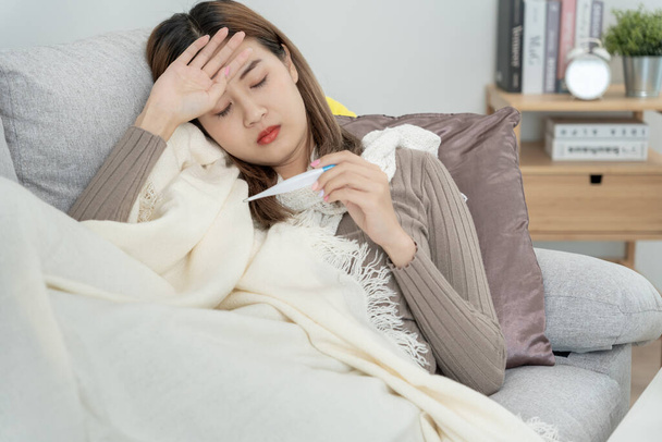 季節性インフルエンザ、アレルギー、デジタル温度計、ウイルス、コロナウイルス、病気、呼吸器で体温、女性のくしゃみや鼻水をチェックしながら、高熱を持っている若いアジアの女性 - 写真・画像