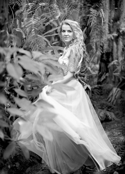 Foto en blanco y negro de una chica impresionante en un vestido de novia, rubia con rizos largos dando vueltas en la naturaleza. Concepto de felicidad - Foto, imagen