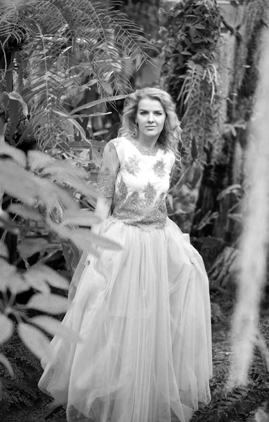Zwart-wit foto van een prachtig meisje in een trouwjurk, blond met lange krullen poseren in de natuur. Vrouwenconcept - Foto, afbeelding