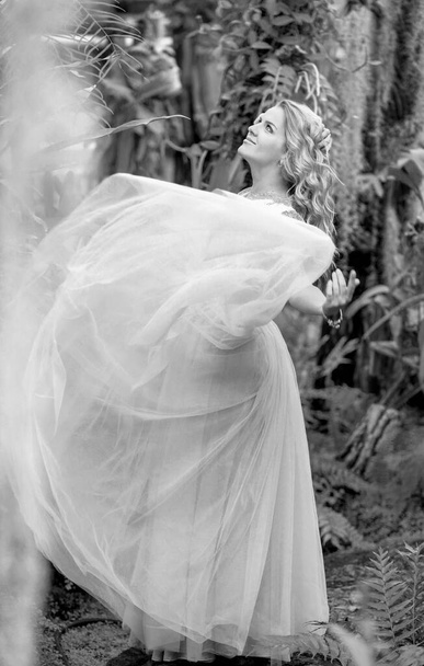 Foto en blanco y negro de una chica impresionante en un vestido de novia, rubia con rizos largos dando vueltas en la naturaleza. Concepto de felicidad - Foto, imagen