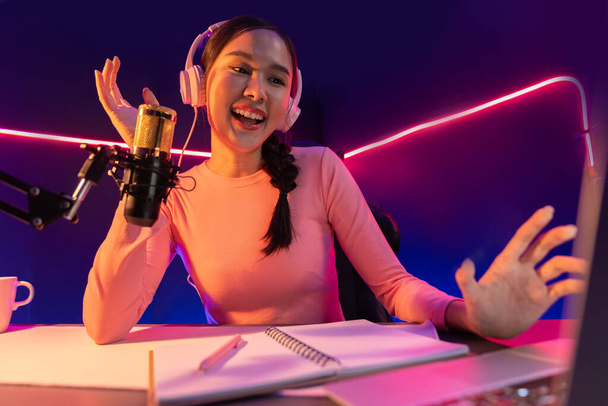 Hymyilevä luova nuori kaunis aasialainen vaikuttaja puhuu kanava positiivinen podcast puheen yöllä, käyttäen kannettavaa tietokonetta esitykseen verkossa vaaleanpunainen neon valo moderni studio. Stratagem. - Valokuva, kuva