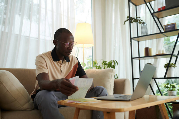 Homem preto verificando contas de serviços públicos ao gerenciar suas despesas através do aplicativo no laptop - Foto, Imagem