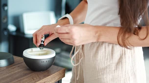 Женщина добавляет масло в серый ароматический диффузор на светлый стол дома, включая освежитель воздуха. Высококачественные 4k кадры - Кадры, видео
