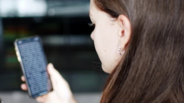 Młoda uśmiechnięta kobieta czyta zabawną książkę online na swoim smartfonie. Wysokiej jakości materiał 4k - Materiał filmowy, wideo