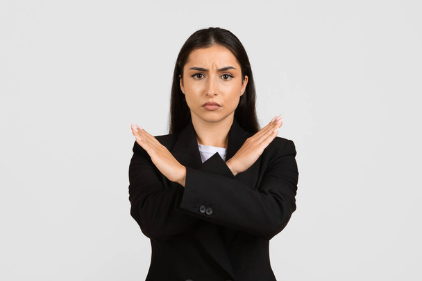Femme d'affaires professionnelle en costume noir faisant fermement un geste négatif, croisant les bras pour indiquer un refus strict ou fixant des limites dans le contexte des affaires - Photo, image