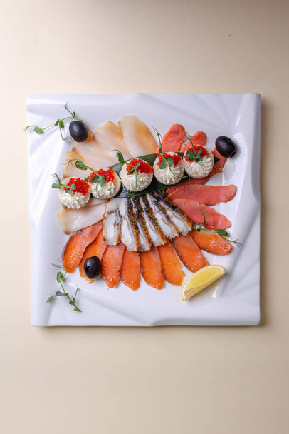 Un plato ingeniosamente organizado de mariscos frescos salmón, trucha, caviar y camarones en un plato blanco con rodajas de limón y verduras. Una composición de naturaleza muerta visualmente atractiva. - Foto, imagen
