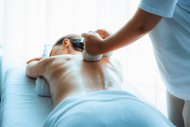 Heiße Kräuterball-Wellness-Massage Körperbehandlung, Masseur sanft komprimiert Kräuterbeutel auf Frauenkörper. Ruhe und Gelassenheit der Aromatherapie Erholung in Tageslicht Ambiente im Wellness-Salon. Ruhige Lage - Foto, Bild