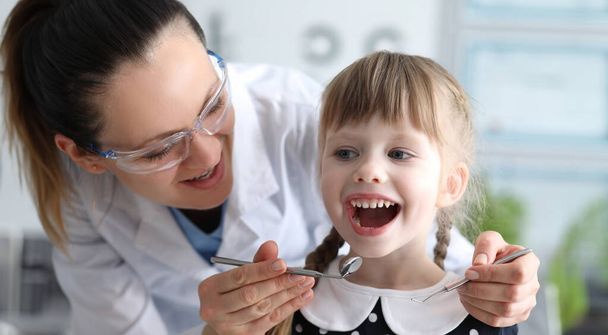 La mujer dentista examina los dientes en la clínica al niño. El médico controlará la higiene dental en el hogar. Dentista llevará a cabo formación adicional, higiene en el hogar. Garantía para rellenos antes de cambios en los dientes
 - Foto, imagen