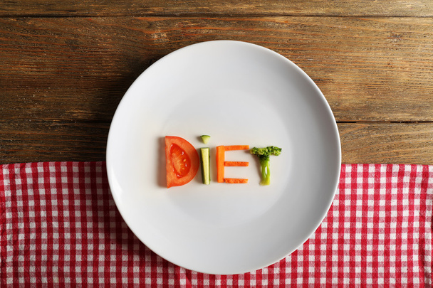 Word DIET made of sliced vegetables in white plate with napkin on wooden background - Foto, immagini