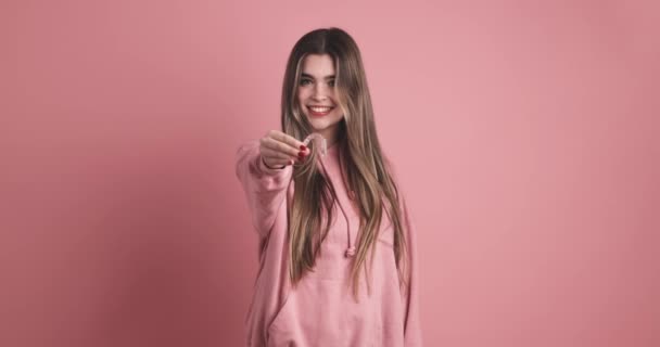Retrato de una joven sonriente vestida con ropa casual con el pelo largo y oscuro sosteniendo al alineador dental transparente y mirando a la cámara sobre un fondo rosado - Metraje, vídeo