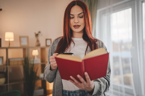 giovane donna adulta una studentessa leggere libro o studiare a casa capelli rossi copia spazio - Foto, immagini