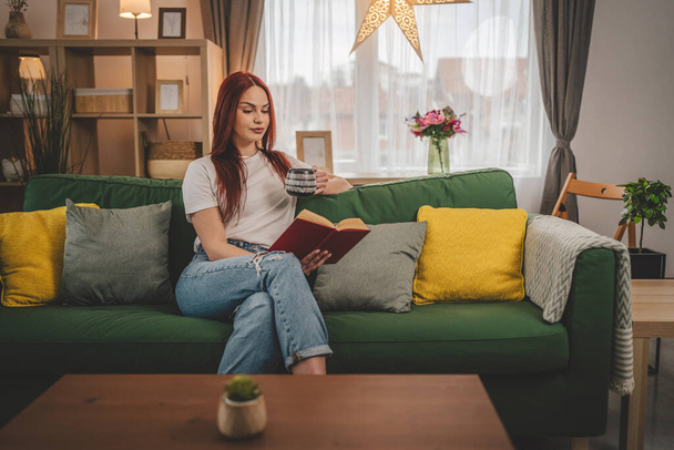 jeune femme adulte une étudiante lit un livre ou étudie à la maison espace de copie de cheveux rouges - Photo, image