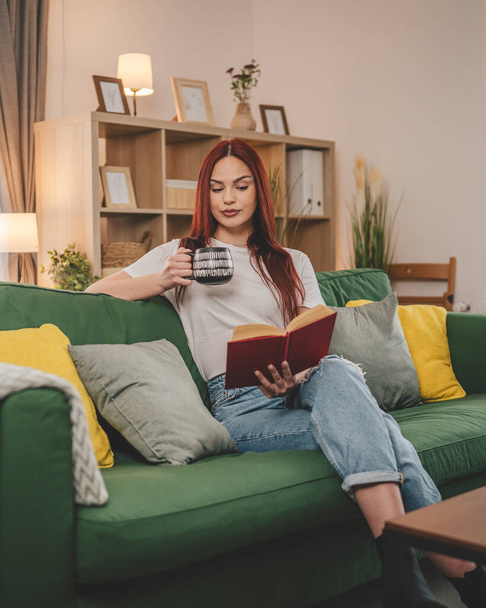 νεαρή ενήλικη γυναίκα μία φοιτήτρια διαβάζει βιβλίο ή σπουδάζει στο σπίτι κόκκινα μαλλιά αντίγραφο χώρο - Φωτογραφία, εικόνα
