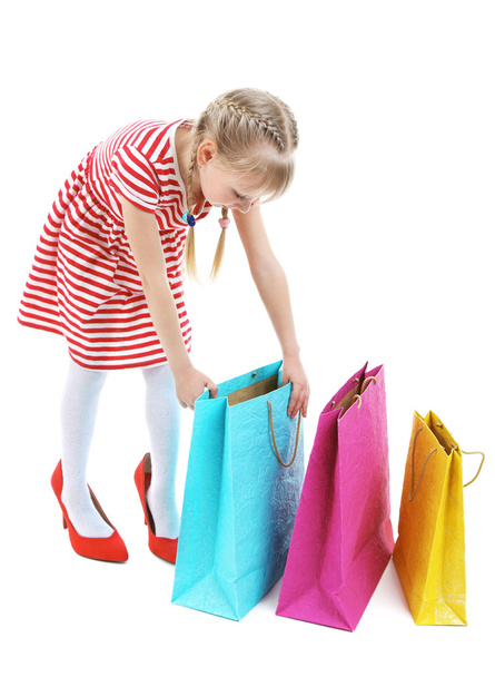 Hermosa niña en los zapatos de mamá con bolsas de compras aisladas en blanco
 - Foto, Imagen