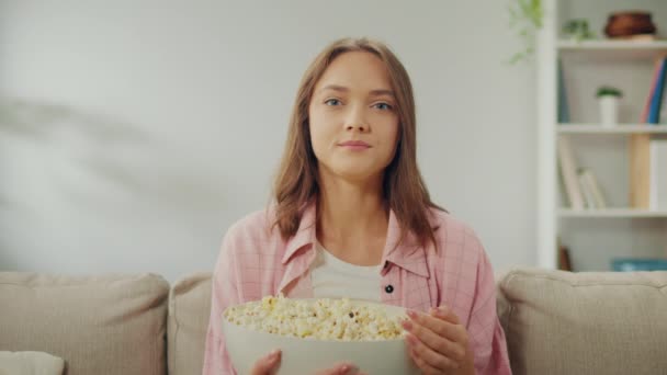 A Happy Young Woman Sitting on the Sofa, Eating Popcorn nd Watching TV. Cheerful Woman Watching a Romantic Movie. A Movie That Will Help Improve Your Mood. Watching a Movie and Its Impact. - Footage, Video