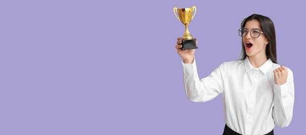 Feliz joven empresaria con copa de trofeo sobre fondo lila con espacio para el texto - Foto, imagen